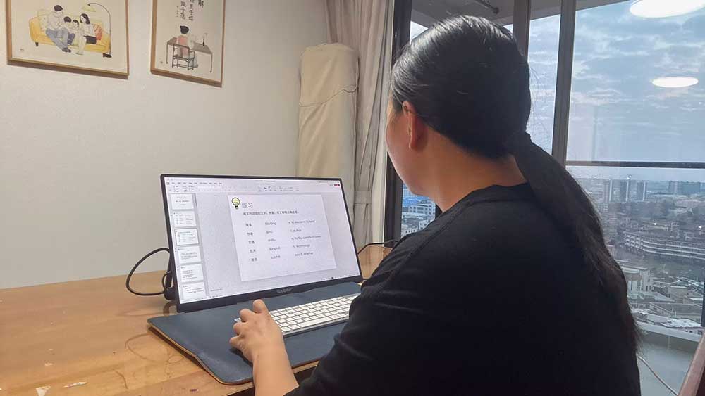 Mandarin tutor Candice reviewing PPT teaching materials on her laptop for an online Chinese class.