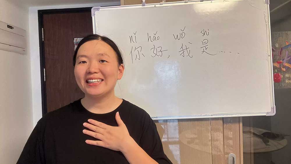 Mandarin tutor Candice teaching greetings and simple self-introductions in front of a whiteboard.